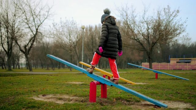 Little girl in jacket riding on swing in autumn city park