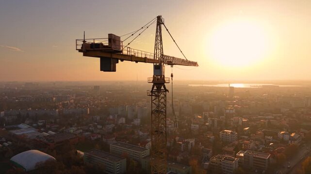 Aerial drone footage of a tower crane operating above a modern high-rise construction site with a panoramic city skyline in the background. The scene showcases urban development, commercial real estat
