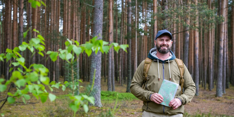 Mature bearded man with backpack stands in pine woodland and looks at camera during calm solo forest walk. Outdoor recreation and walking in nature concept © Dmitrii Masquerade