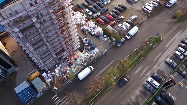 Oblique aerial view of a scaffolded building beside a street and parking area, with piles of construction debris and bags around the base.