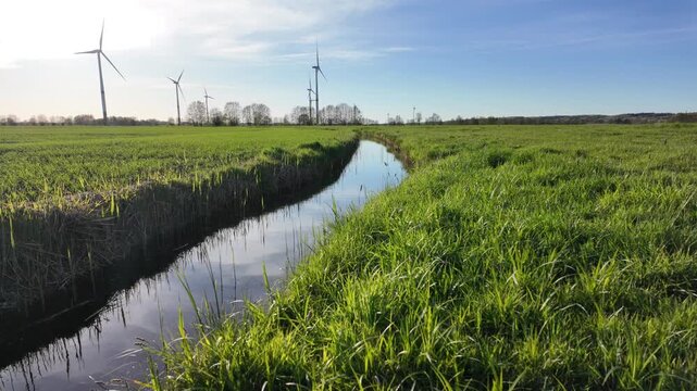 A serene rural landscape with a stream flowing through a green meadow and wind turbines on the horizon, sustainable energy concept.