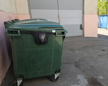 Green waste dumpster behind office building on city street, commercial garbage disposal, urban sanitation service