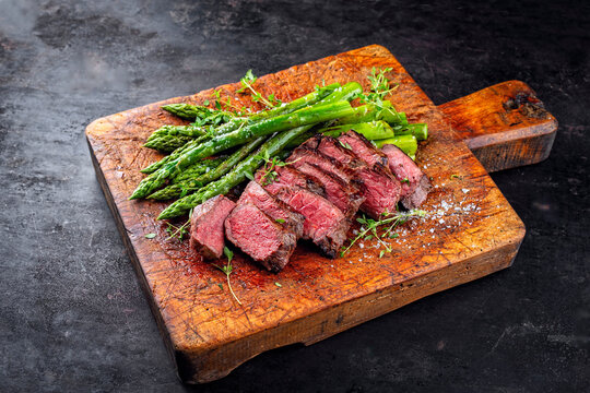 English medium broiled tagliata di manzo beef steak meat with grilled green asparagus served as close-up on rustic wooden board