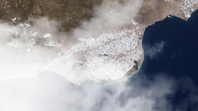 Flying over Almeria coastline and vast greenhouse agriculture landscape with passing clouds satellite view from space based on Nasa imagery