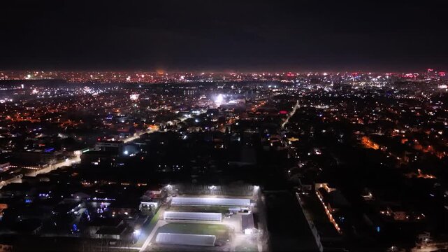 Night aerial view of a city with fireworks, runway lights, and a brightly lit urban neighborhood in the foreground. New eyar's celebration seen from the skies!