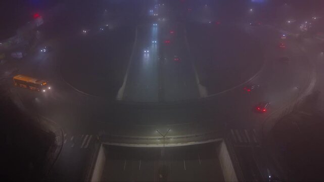 Nighttime underpass or trench-style highway with light traffic, viewed from above in foggy low-light conditions