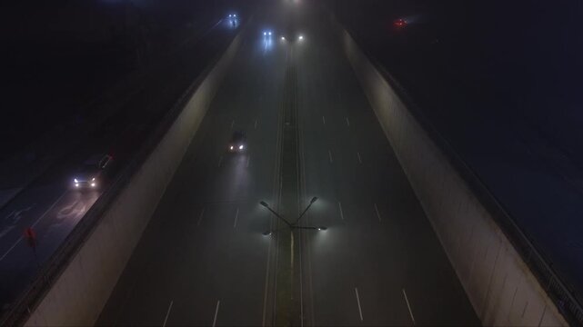 Nighttime underpass or trench-style highway with light traffic, viewed from above in foggy low-light conditions