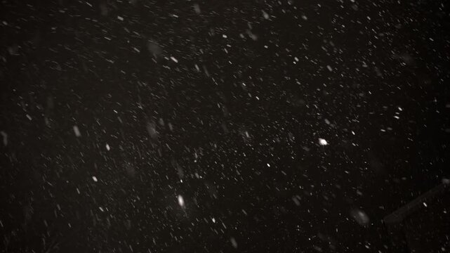 Experience the beauty of a snowstorm at night as snow cascades from the heavens, swirling gently against a mysterious black canvas, creating a serene winter ambiance