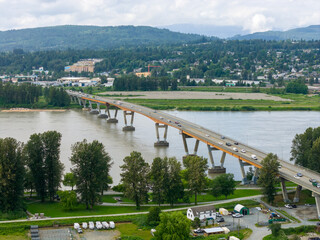 Fototapeta premium Aerial View of Bridge Crossing River With Suburban Landscape and Distant Forested Hills in BC