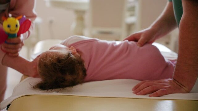 A colorful baby rattle is gently presented to an infant, while caregiver is performing mobility exercises