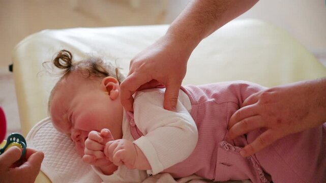 A colorful baby rattle is gently presented to an infant, while caregiver is performing mobility exercises