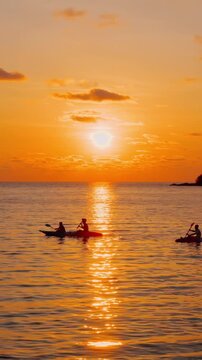 Tropical beach with palm tree and silhouette travel people on kayak in ocean on background colorful sunset. Summer holidays in tropical paradise concept