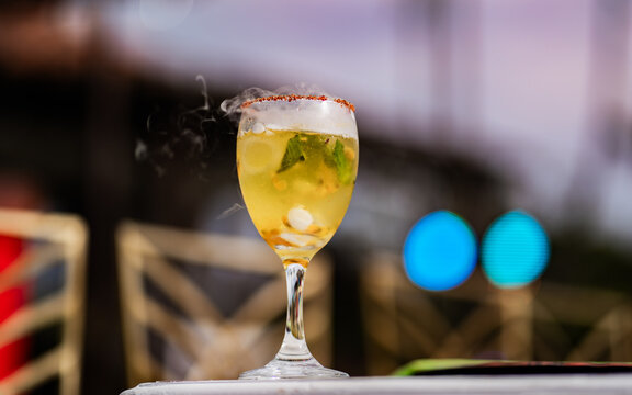 C&oacute;ctel gourmet con efecto de humo, hielo y hojas de menta en copa elegante sobre fondo desenfocado