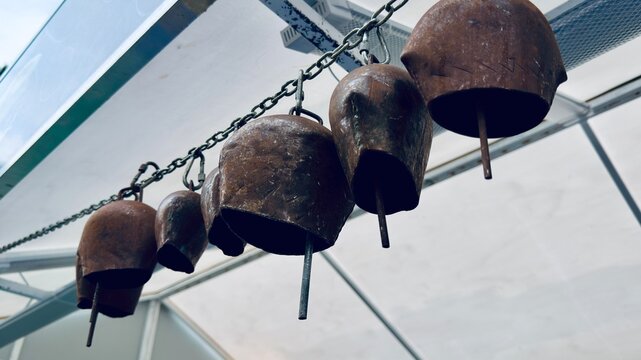 Antique metal cowbells hanging on a heavy iron chain at Eyup Sultan Mosque courtyard in Istanbul, Turkey. Ancient Ottoman empire buildings architecture, decorative elements and cloudy sky view.
