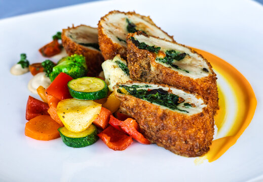 Chicken roulade with spinach filling and roasted vegetables on white plate