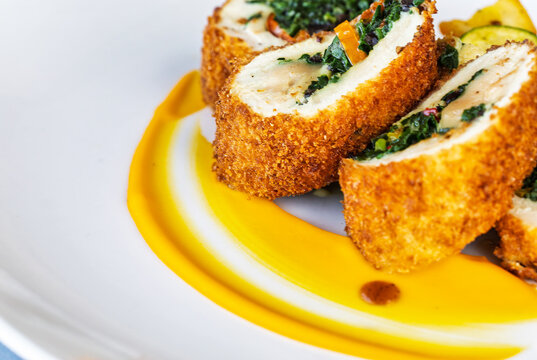 Chicken roulade with spinach filling and roasted vegetables on white plate