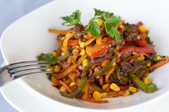 Beef sizzling strips with stir fried vegetables in white bowl with silver fork.