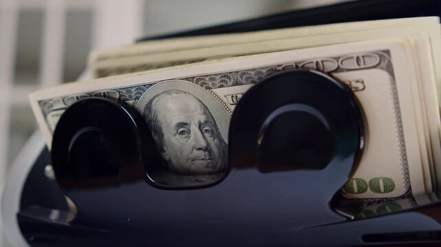 In a chic urban environment at sunset, lush green reflections play over a sleek cash dispenser as crisp hundred-dollar bills elegantly slide out, demonstrating advanced technology