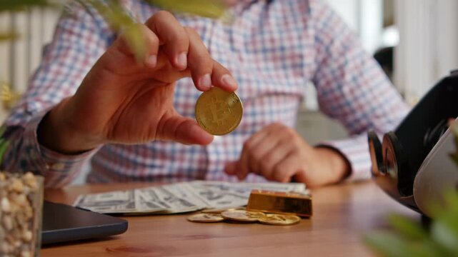 Hands showcase shiny gold coins as a person explores cryptocurrency options while sitting comfortably at a wooden table surrounded by cash and a laptop