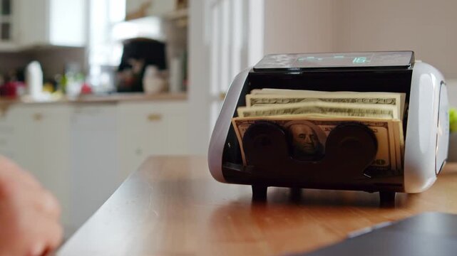 Hands skillfully operate a cash counting machine, stacking bills neatly while sunlight streams through a window, creating a warm and inviting atmosphere
