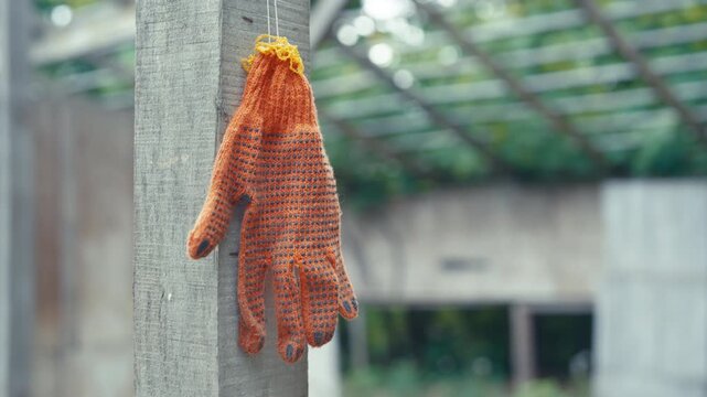 Orange Knitted Work Glove Hanging on Wooden Post at Construction Site | Slow Motion Parallax Close-Up | Labor Safety and Gardening Concept