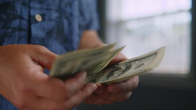 Hands carefully sort through fresh cash, feeling the texture of the bills while light dances through the window, creating a moment of calm reflection