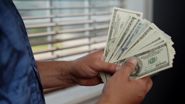 Hands skillfully sort and count stacks of cash, showcasing the crisp bills against the serene background of soft evening light streaming through the window