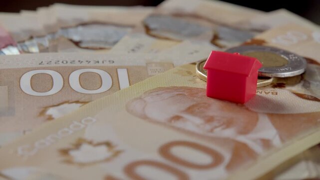 Colorful houses rest on a bed of Canadian bills and coins, bringing a sense of playfulness and creativity to a quiet afternoon filled with dreams of home