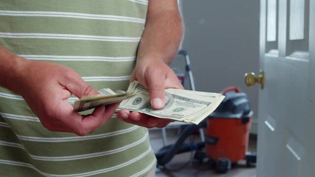 A man carefully counts dollar bills, thinking about how much money he needs for home repairs. He evaluates materials to enhance his living environment with care and thoughtfulness