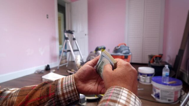 A man carefully counts dollar bills, estimating the expenses for home renovation materials in a room ready for updates and fresh ideas