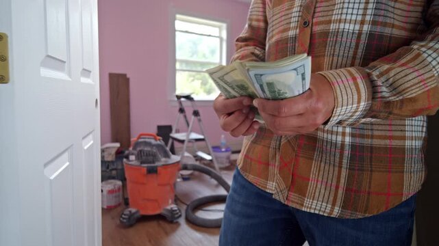 A man is focused on counting dollar bills to determine the budget for materials needed for his home renovation. The atmosphere reflects preparation and planning