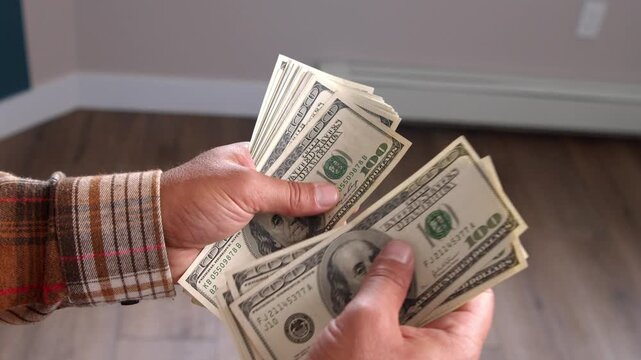 A man carefully counts dollar bills, calculating how much he needs for materials to renovate his home. He focuses intently on making sure he has enough funds