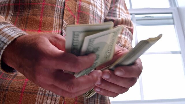 A man meticulously counts dollar bills while planning for home renovation materials, ensuring he budgets wisely for a successful project