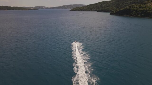High-altitude drone footage following a jet ski speeding through the crystal-clear waters of Lefkada. Scenic islands, open sea and a long wake create a dynamic summer adventure scene in Greece.