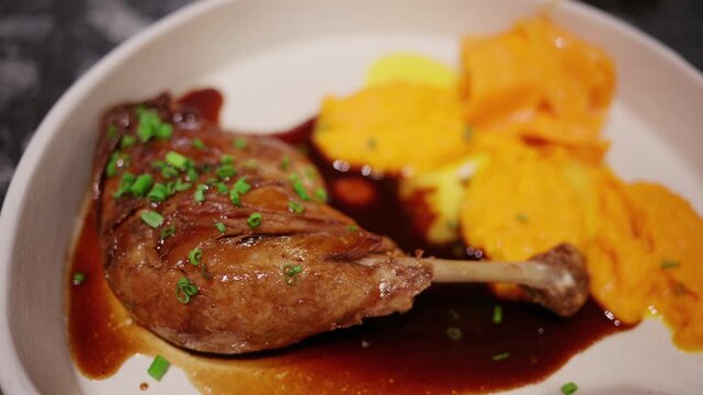 Close up of a gourmet roasted duck leg served with silky carrot puree and rich brown sauce in a modern restaurant setting