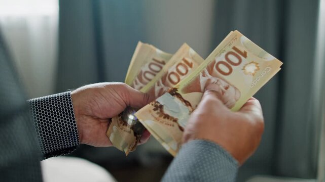Hands skillfully sort and count crisp Canadian dollars in a warmly lit room, showcasing the elegance of money management and attentive focus on detail