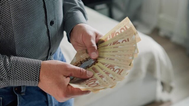 Hands skillfully manipulate Canadian dollars in a sunlit room. Each note reveals the beauty of currency as the man counts them with care and focus, immersed in a financial moment