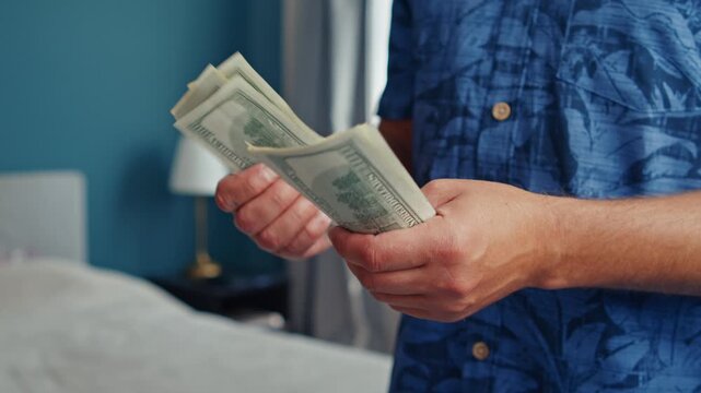 A man in a vibrant blue shirt counts crisp bills in a charming bedroom, feeling a mix of joy and anticipation as he prepares for a special moment