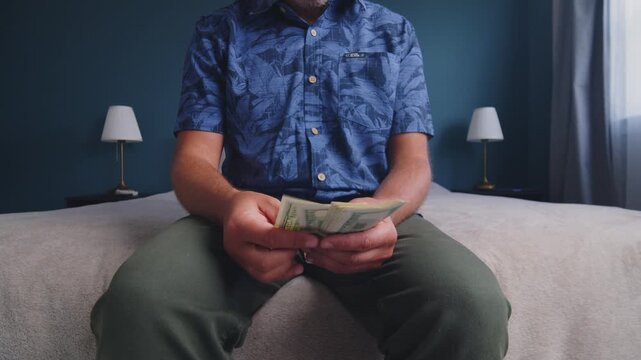 A young person sits on a soft bed in a cozy blue room, counting crisp bills with focused hands, surrounded by calm, soothing light