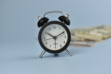Silver alarm clock stands beside folded bills © Nazir