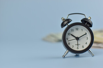 Silver alarm clock stands beside folded bills © Nazir