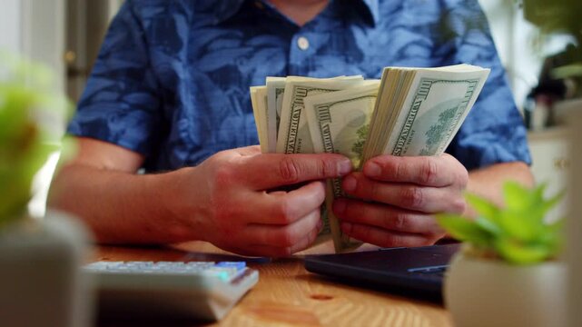 Hands deftly sort crisp bills on a wooden table, surrounded by potted plants and a laptop, creating a tranquil and productive atmosphere for budgeting
