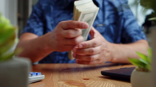 Hands skillfully unite crisp dollar bills at a charming table filled with greenery. Light pours in as each note is counted with care, bringing a sense of focus and warmth