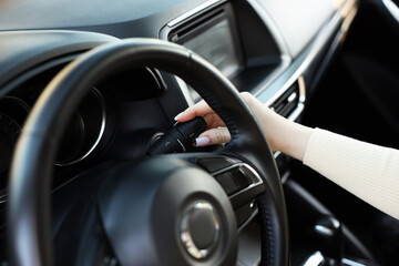 Obraz premium Woman turning windshield wiper switch behind steering wheel of modern car, closeup