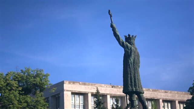 Stephen the Great statue against a vivid blue sky, with trees and urban architecture in the background, Chisinau, Moldova
