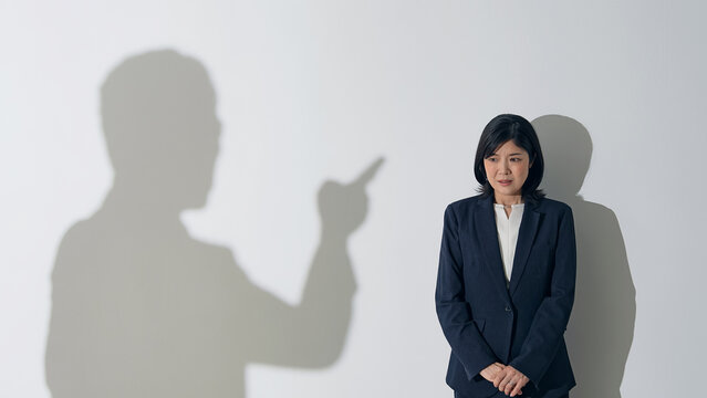 男性のシルエットに叱責される女性ビジネスパーソン