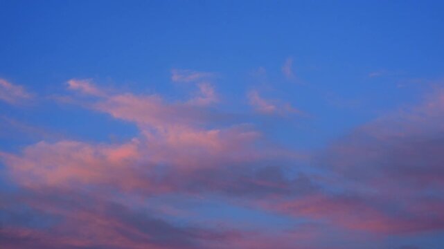 Soft pink and blue clouds spreading across the evening sky above urban buildings and communication antennas
