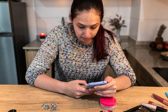 Concentrated redhead following a phone reference while preparing special effects makeup