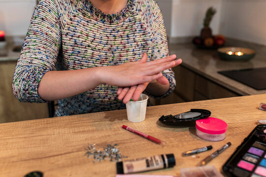 Costumed woman reaching for cosmetics spread across a wooden table at home
