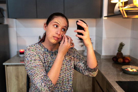 Redhead model blending a fake wound on her cheek using a phone screen mirror